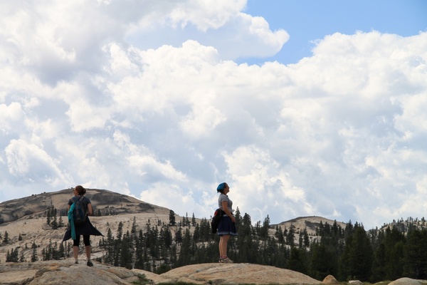 2 women standing on rocks under sky of clouds