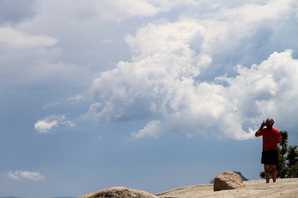 elderly man standing on rock under sky with puffy clouds