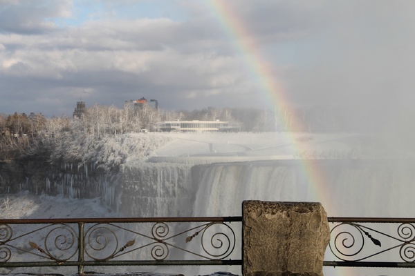 railing in front of rainbow over frozen niagara falls