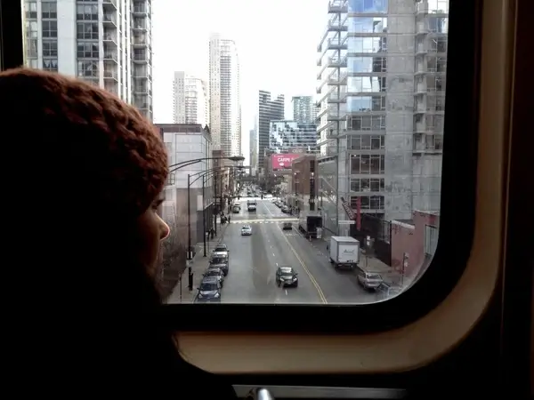 girl in beanie hat peering at downtown city on train
