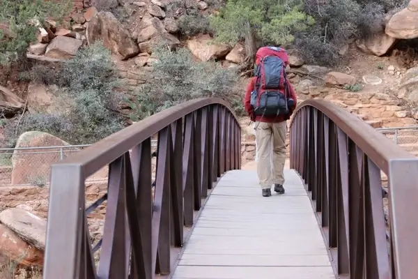 man with hiking backpack walking across bridge