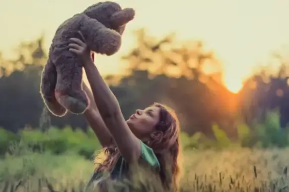 joyful woman with teddy bear under sunlight