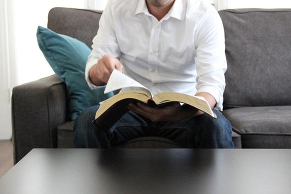 man on couch turning page of bible