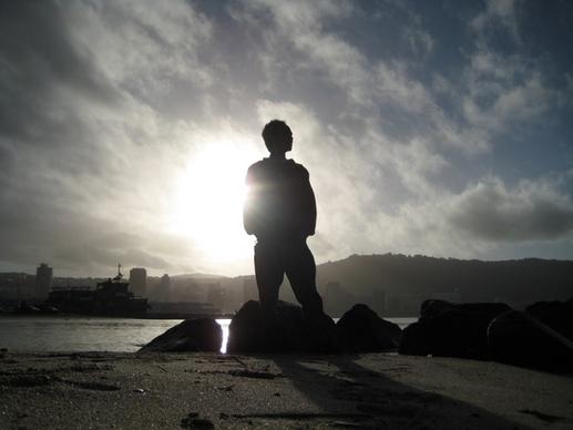 silhouette of man standing on beach against city