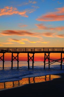 wooden bridge on calm beach at sunset
