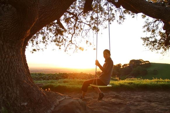 woman on swing under tree at sunrise